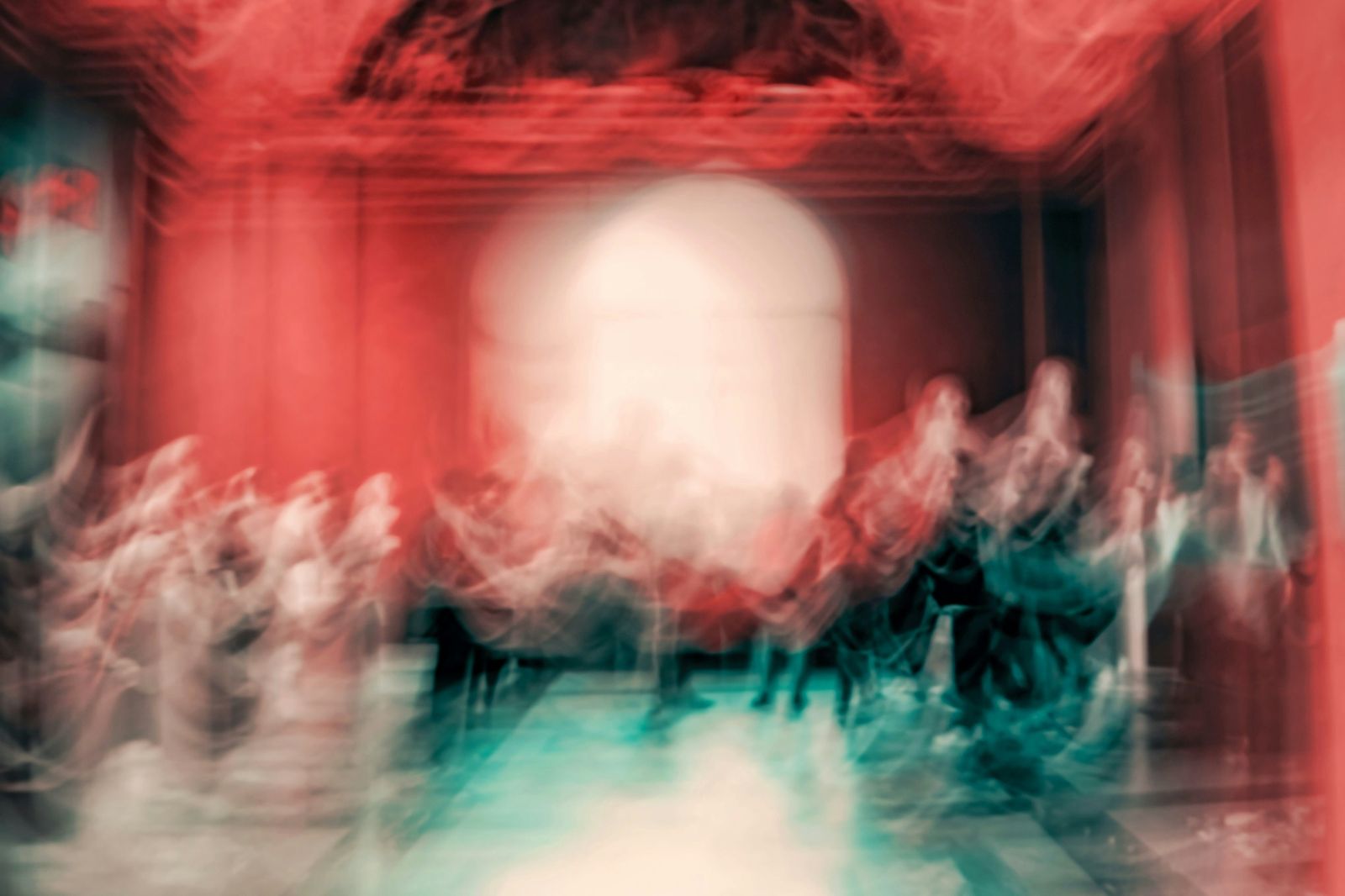 Long-exposure photo of people moving through a red-lit theatre hall